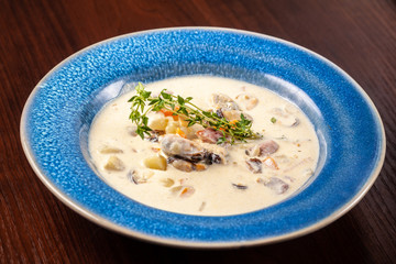 The concept of Italian cuisine. Creamy soup with seafood, mussels, potatoes, carrots, thyme. serve in a blue plate.