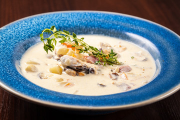 The concept of Italian cuisine. Creamy soup with seafood, mussels, potatoes, carrots, thyme. serve in a blue plate.