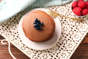 Plate with tasty chocolate pancakes and berries on tray