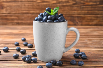 Cup with ripe blueberries on wooden table