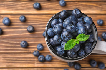 Cup with ripe blueberries on wooden table, top view