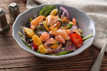 Bowl of delicious vegetable salad with seafood on wooden table