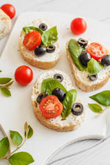 Sandwiches with cream cheese tomatoes, olives and basil on a wooden white board