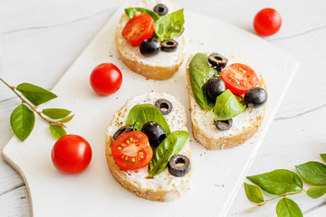 Sandwiches with cream cheese tomatoes, olives and basil on a wooden white board