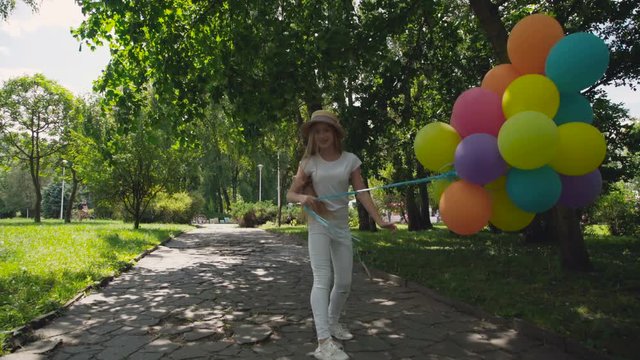 Happy young girl runs in the green sunny park and holds colourful balloons