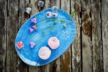 Obraz na płótnie Canvas The marshmallow on a blue sky plate. Light dessert. Delicate wildflowers. And frozen in the ice berries