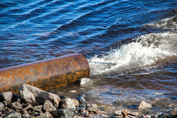 Dirty water flows out of a large metal rusty pipe under pressure into the river.