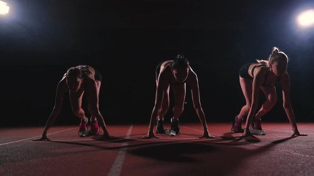 Female runners at athletics track crouching at the starting blocks before a race. In slow motion.