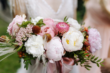 Beautiful wedding bouquet with pink and white flower roses, peonies and greenery in bride hand. Beauty of colored flowers. Close-up. Bridal accessories. Details for marriage.