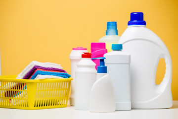 Photo of several bottles of cleaning products and multi-colored towels in basket isolated on orange background