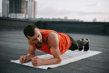 handsome sportsman doing plank on yoga mat on roof