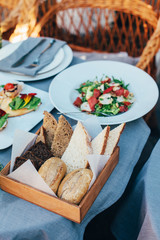 Fresh Italian style salad, served in a white plate, and a basket with bread is located next to it.