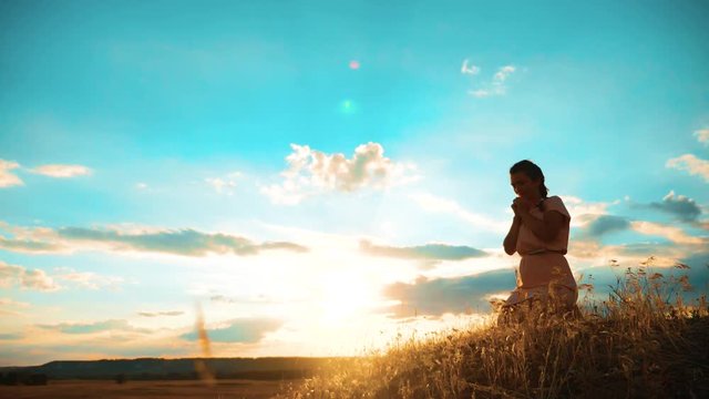 Girl folded her hands in prayer silhouette at sunset. woman praying on her knees. slow motion video. Girl lifestyle folded her hands in prayer pray to God. the girl praying asks forgiveness for sins