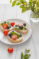 Sandwiches with cream cheese tomatoes, olives and basil on a wooden white board