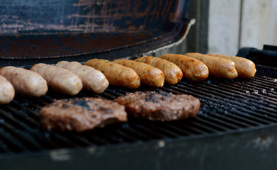 Beefburgers and sausages cooking on an open grill