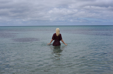 portrait of pretty blonde girl wearing purple dress, posing in a beautiful ocean landscape.