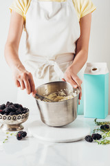 cropped shot of woman in apron preparing cream for cake with whisk