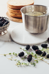 cropped shot of metal bowl with whisk and cream for cake and blackberries on white table