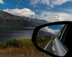 Car mirror reflection on road by the lake