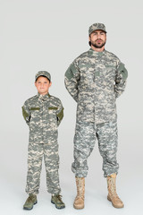 father and son in military uniforms looking at camera on grey background