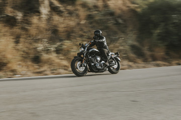 Man in black leather jacket riding a motorcycle on the road across the mountain.