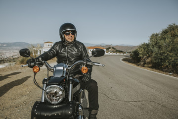 Fototapeta na wymiar Man with black helmet, jacket and sunglasses standing on a classic American motorcycle.