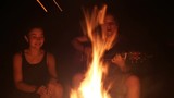 Young friends singing songs with guitar sitting by the campfire at the dark night