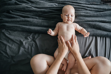 A woman parent makes a belly massage to a newborn baby lying on a gray blanket. view from above.