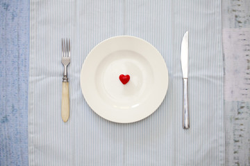 The figure of the heart lies on a round white plate set with a knife and fork on a napkin 