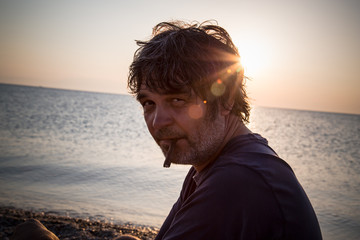 Handsome man relaxing on the beach in Greece while sunsets / Portrait of handsome middle aged man