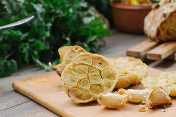 Baked knob of garlic on a wooden plate with cloves of garlic beside it.