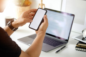 Cropped shot of man using mobile phone while working with laptop on desk.