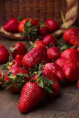 Bunch of red, fresh, washed strawberries on a wooden table spilled from a wooden basket.