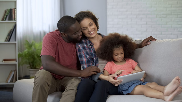 Parents And Little Daughter Watching Cartoons On Tablet, Family Happy Together