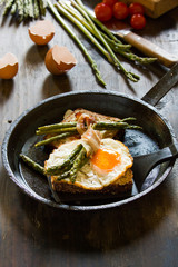 Delicious fried eggs on a toasted bread in a metal pan with grilled asparagus wrapped in fried bacon.