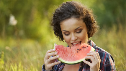 Beautiful lady eating fresh and juicy watermelon sitting in park, healthy food