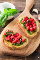 Bruschetta with fresh pesto, basil leaves and tomatoes. Wooden background