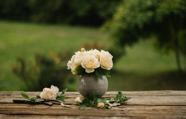 Lovely bouquet of white roses in a grey vase on a rustic wooden table. Shallow depth of field, soft...
