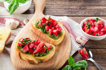 Bruschetta with fresh pesto, basil leaves and tomatoes. Wooden background