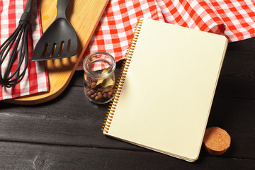 Blank sheet of opened notepad and kitchen utensils on  table with tablecloth, copy space
