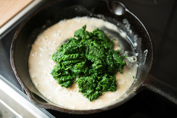 Preparation of a dish - baby spinach boiled in garlic sauce in a cast-iron pan.