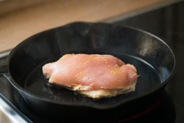 One of the steps in preparation of a raw stuffed chicken breast in a cast-iron pan ; grilling the meat.
