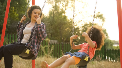 Young babysitter playing with carefree kid, swinging outdoor at child playground