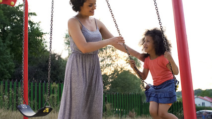 Beautiful smiling mother in grey dress swinging her favorite giggling daughter