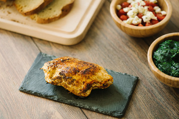 Grilled, stuffed chicken breast on a stone plate with homemade bread, salad and spinach as side dish.