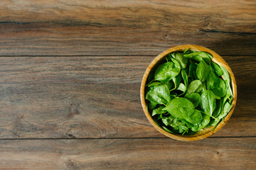 Fresh, raw baby spinach in a wooden bowl on wooden background, from above.