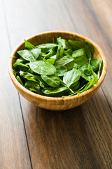 Fresh, raw baby spinach in a wooden bowl on wooden background, from above.