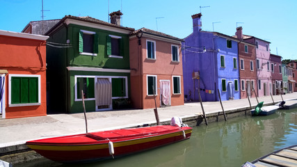 Fototapeta na wymiar Red motorboat parked on Venetian canal, beautiful colorful houses, Burano