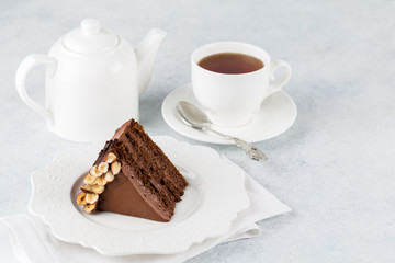 A piece of chocolate cake with nuts on light background and cup of tea. Copy space