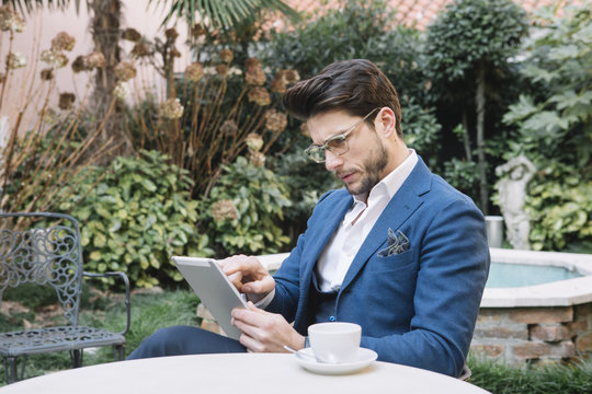 Elegant businessman using tablet in garden cafe